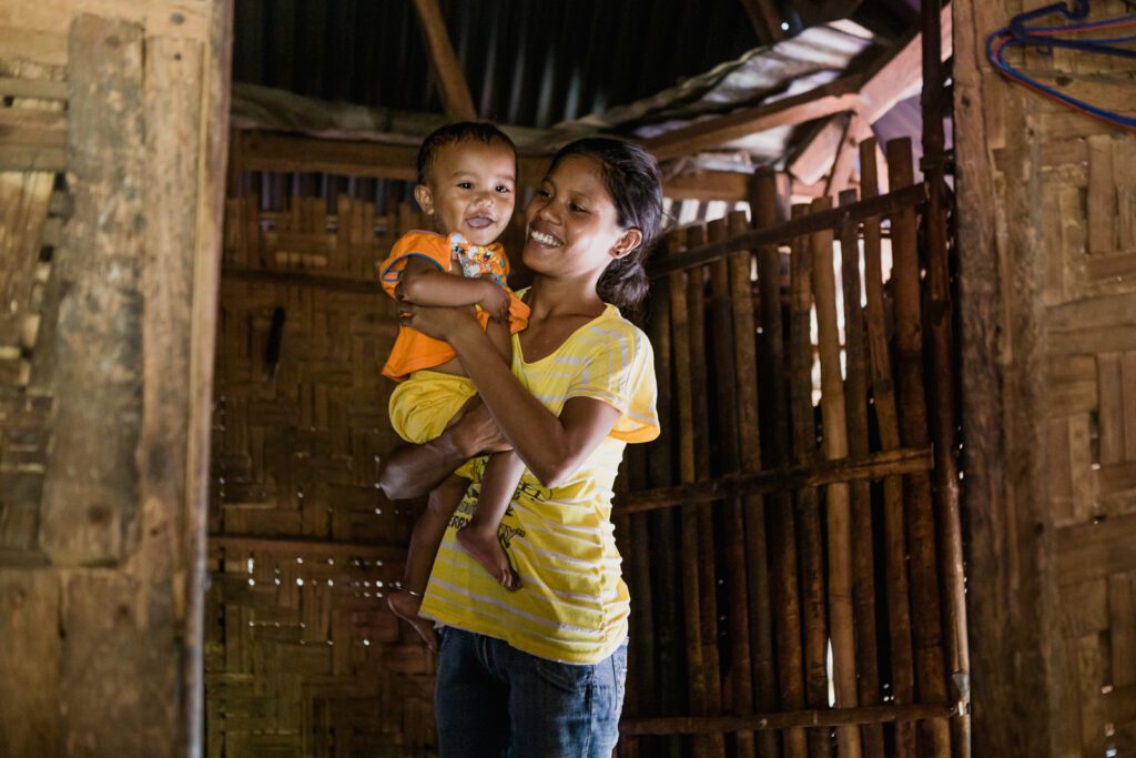 A mother in a yellow shirt holds her smiling child.